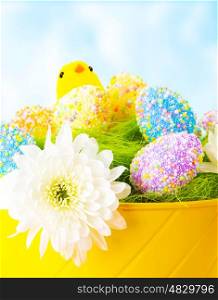 Closeup of colorful Easter eggs with chick toy in festive basket over blue sky background, traditional Christian celebration
