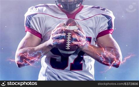 closeup of confident American football player holding ball while standing on field at night