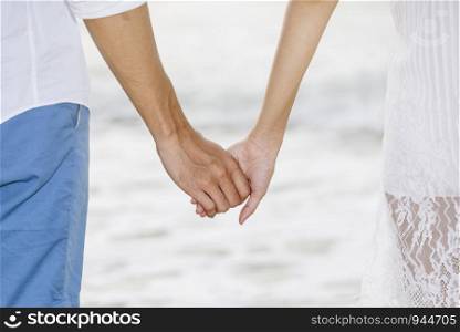Closeup of couple holding hands togethers while walking on the beach at sunset. Love and valentine concept.