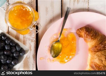 Closeup of croissant, blueberries and orange jam over a wooden table seen from above. Closeup of croissant and orange jam over a wooden table