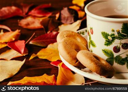 Closeup of cup of tea with biscuits and autumnal foliage over a dark table. Closeup of cup of tea with biscuits and autumnal foliage