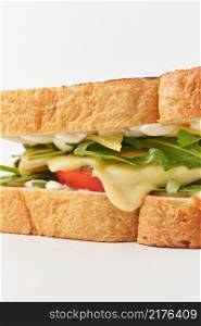 Closeup of delicious melted yellow cheese and arugula leaves between crunchy white bread toasted slices with golden crust placed on white background. Golden sandwich with vegetables and cheese