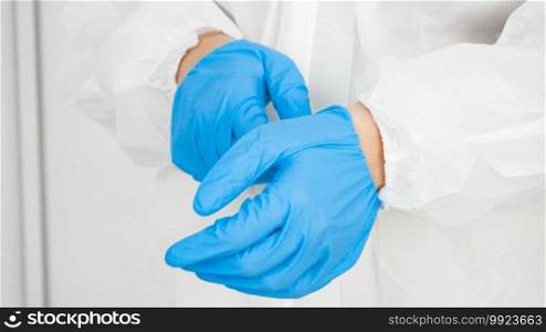 Closeup of doctor in protective biohazard suit wearing and putting on protective blue rubber gloves in hospital.. Closeup of doctor in protective biohazard suit wearing and putting on protective blue rubber gloves in hospital
