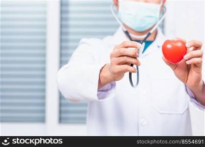 Closeup of doctor man wearing white coat standing holds his stethoscope on hand for listening examining red heart, person showing medical equipment