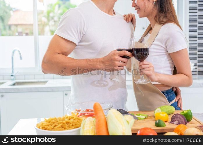 Closeup of drinking wine on happy Asian young married couple hands in home kitchen. Boyfriend and girlfriend cooking together. People lifestyle and romantic relationship concept. Valentines day