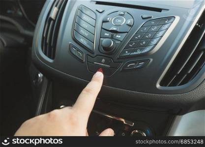 Closeup of driver pressing emergency button on car dashboard