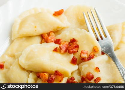 Closeup of dumplings sprinkled with pork scratchings with fork as food background. Traditional polish (Poland) cuisine.