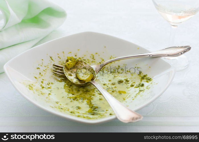 Closeup of eaten linguine pasta plate with pesto genovese, potatoes and white wine glass. Closeup of eaten linguine pasta plate with pesto genovese and potatoes