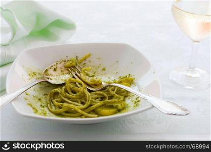 Closeup of eaten linguine pasta with pesto genovese, potatoes and white wine glass. Closeup of eaten linguine pasta with pesto genovese and potatoes
