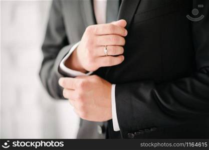Closeup of elegant young fashion man dressing up for wedding celebration. Color close up image of male hands. Handsome groom dressed in modern blue formal suit. Man in suit with hand adjusts sleeve of shirt close-up. Close up of business professional buttoning up his shirt sleeves.