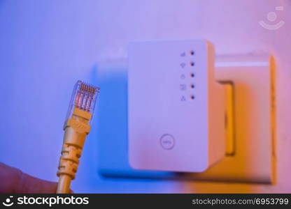 Closeup of ethernet cable. WiFi extender device in electrical socket on the wall on the background. The device is in access point mode that help to extend wireless network in home or office.