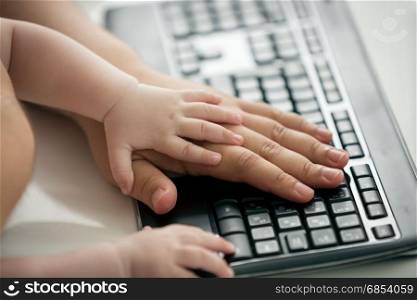 Closeup of fathers and baby&rsquo;s hands on computer keyboard