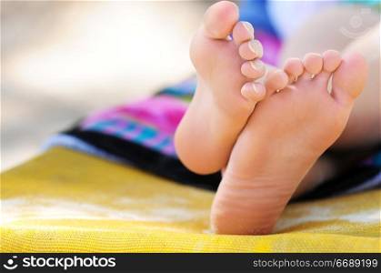 Closeup of feet of a young girl in chaise lounge relaxing on a beach