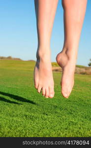 closeup of feet of jumping on green field woman