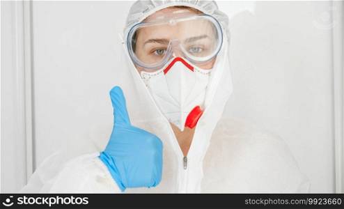Closeup of female doctor wearing protective suit, mask, gloves and goggles showing thumbs up. Positive emotion of medical worker fighting against covid-19 and coronavirus.. Closeup of female doctor wearing protective suit, mask, gloves and goggles showing thumbs up. Positive emotion of medical worker fighting against covid-19 and coronavirus