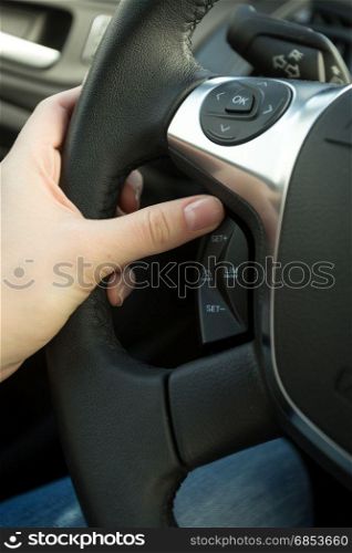 Closeup of female driver adjusting cruise control system on steering wheel