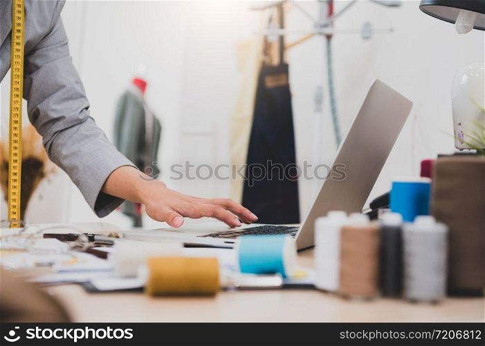Closeup of female fashion designer hand working in clothing shop studio and using laptop computer to contact customer. Woman creating design new collection . Tailor sewing. People lifestyle concept