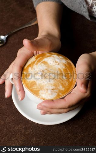 Closeup of female hands holding cup of Cappuccino