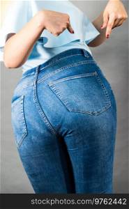 Closeup of female plus size hips buttocks wearing blue jeans, woman presenting fashionable outfit. Fashion clothing femininity concept. Gray background. Woman hips buttocks in jeans clothing