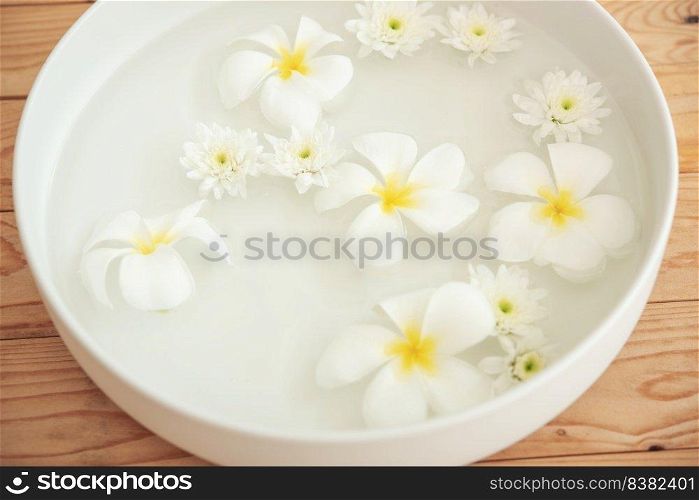 closeup of frangipani flowers and chrysanthemum floating in bowl of water at wellness center. white flowers in ceramic bowl with water for aroma therapy at spa. spa setting for beauty treatment.
