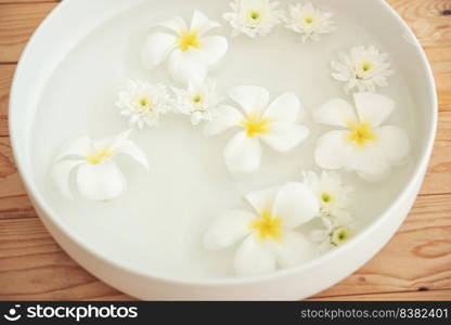 closeup of frangipani flowers and chrysanthemum floating in bowl of water at wellness center. white flowers in ceramic bowl with water for aroma therapy at spa. spa setting for beauty treatment.