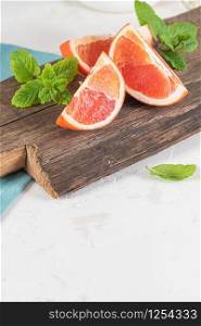 Closeup of fresh juice grapefruit with green sappy leaves of mint, refreshing fruits and herbs on wooden board