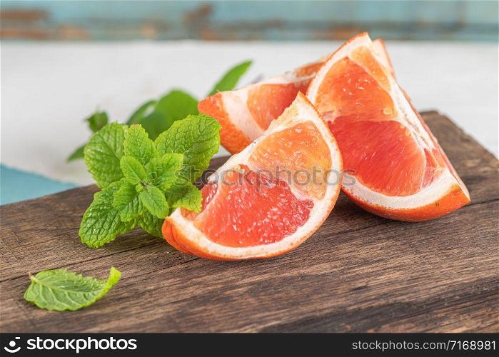 Closeup of fresh juice grapefruit with green sappy leaves of mint, refreshing fruits and herbs on wooden board