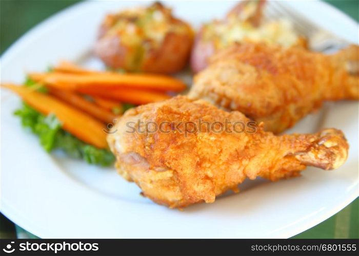 Closeup of fried chicken legs with roasted carrots and crushed potatoes