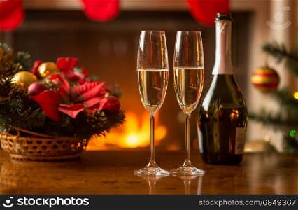 Closeup of glasses of champagne on table next to old clock showing midnight at living room decorated for Christmas