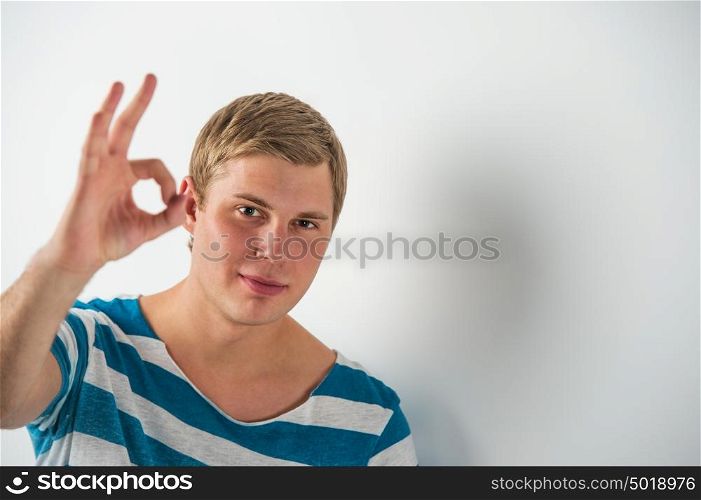 Closeup of good looking young man gesturing okay sign while leaning on white wall