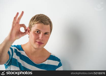 Closeup of good looking young man gesturing okay sign while leaning on white wall