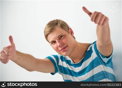 Closeup of good looking young man gesturing thumbs up sign while leaning on white wall