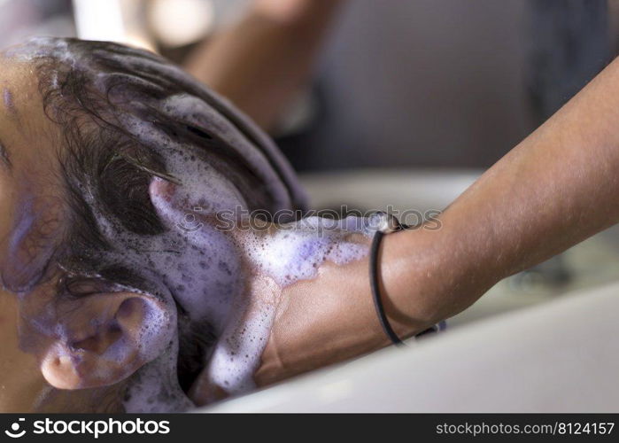 Closeup of hairdresser’s hands washing hair of a girl in hair salon.