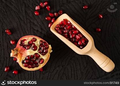 Closeup of half pomegranate fruit and bailer with seeds inside seen from above over a black textured background. Closeup of half pomegranate fruit and bailer with seeds inside seen from above