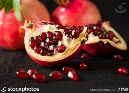 Closeup of half pomegranate fruit and seeds on a black textured background. Closeup of half pomegranate fruit and seeds