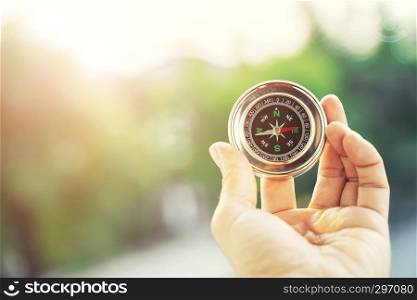 Closeup of hand holding compass with blurred green nature and sunlight with flare background with free copy space for text. Life, travel and guide for success concept.