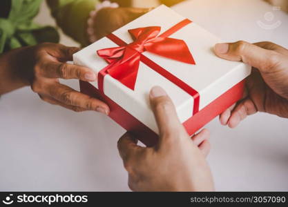 Closeup of hands giving gift box with red ribbon in Christmas day and new year festival to each other. Man giving surprise to woman. Holiday and event. Surprising giftbox in dating on end year party