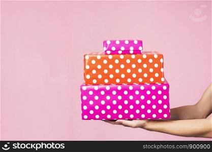 Closeup of hands holding gift boxes in pink background. Holiday concept.