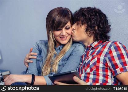 Closeup of handsome man kissing to young beautiful woman and holding electronic tablet in his hand. Love and leisure time concept.. Man kissing to young woman and holding tablet