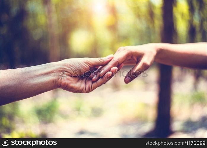 Closeup of helping hand of human during travel in forest. Hand in hand together. Two hands holding for support each others. People and harmony concept. Giving hands for low circumstances suffering
