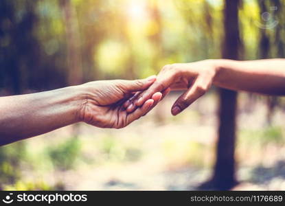 Closeup of helping hand of human during travel in forest. Hand in hand together. Two hands holding for support each others. People and harmony concept. Giving hands for low circumstances suffering