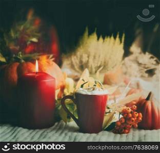 Closeup of hot chocolate with cream in mug and burning candle on white rug. Autumn concept with pumpkin and wild berries. Cozy mood background. Front view. Still life
