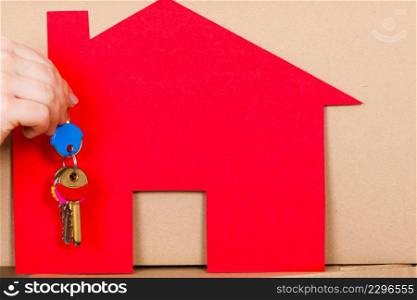 Closeup of human hand holding keys to new apartment. Red paper house and boxes in background. Real estate and housing concept.. Human holding keys to new house apartment.
