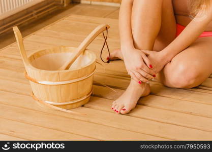 Closeup of human woman legs feet, hands with sauna bucket and ladle. Person relaxing resting in spa.