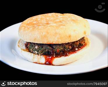 Closeup of juicy hamburger between buns with delicious red sauce on white plate towards black