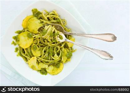 Closeup of linguine pasta with pesto genovese and potatoes over a table with cutlery seen from above. Closeup of linguine pasta with pesto genovese and potatoes over a table