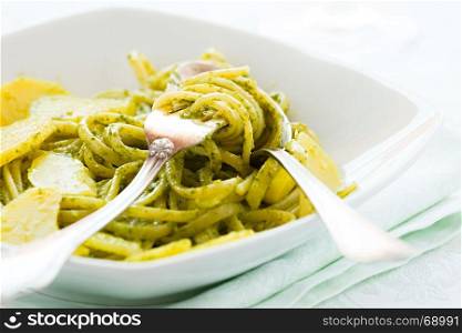 Closeup of linguine pasta with pesto genovese and potatoes over a table with cutlery. Closeup of linguine pasta with pesto genovese and potatoes