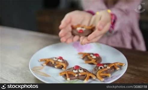 Closeup of little girl&acute;s hands offering christmas decorated homemade cookie over the plate with many sweets. Child&acute;s hands holding tasty chocloate cookie and giving it to the viewer. Dolly shot.