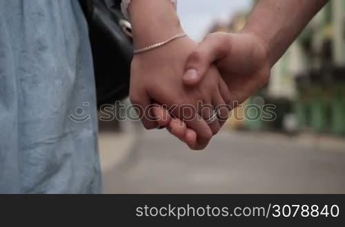 Closeup of loving couple holding hands while walking city street. Young hipsters stepping down street holding hands, expressing love, tenderness and support during romantic date. Slow motion. Steadicam stabilized shot.
