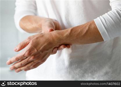 Closeup of male arms holding her painful wrist caused by prolonged work on the computer, laptop. Carpal tunnel syndrome, arthritis, neurological disease concept. Numbness of the hand